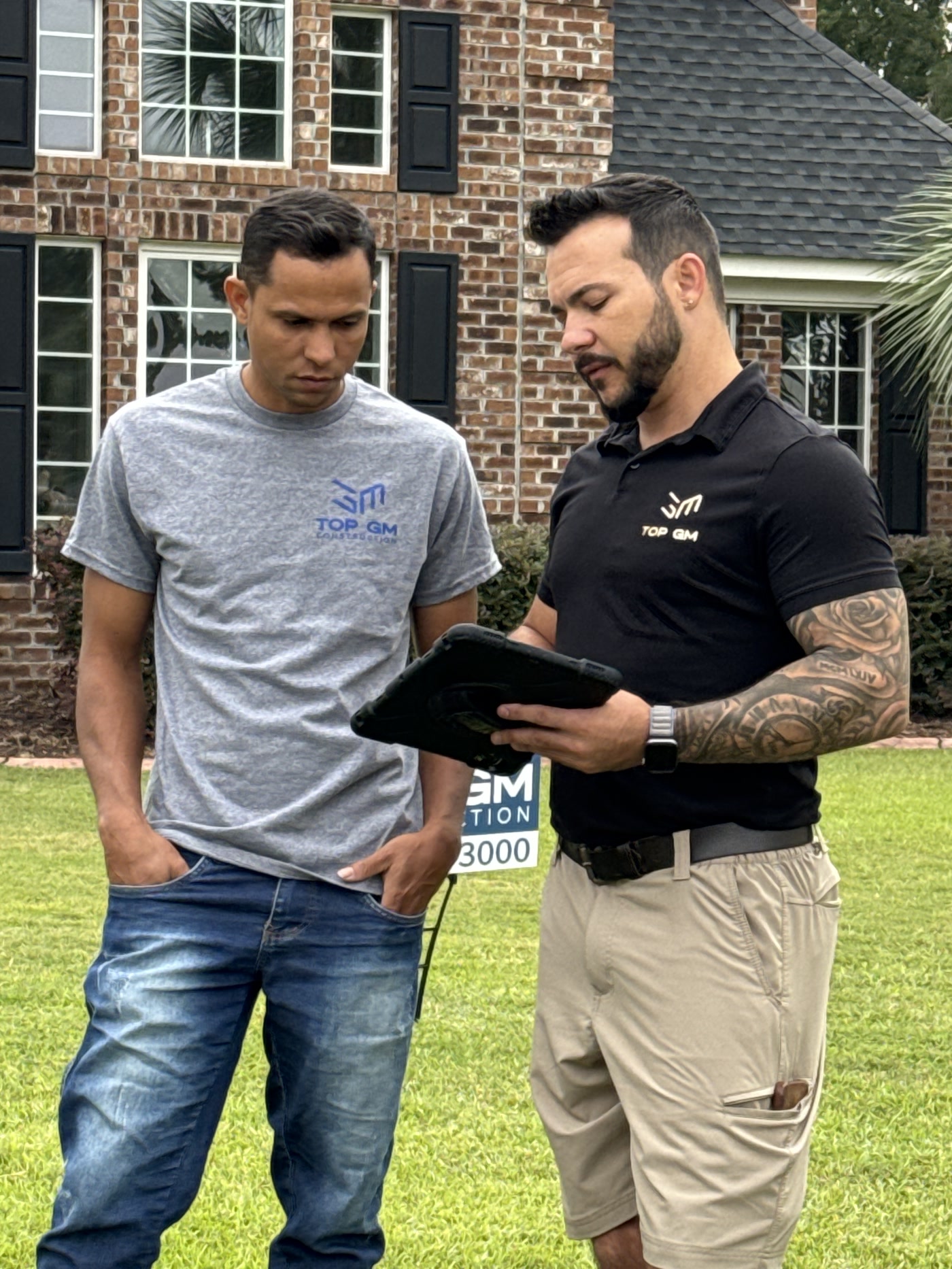 Two Top GM team members reviewing a project on a tablet in front of a brick home